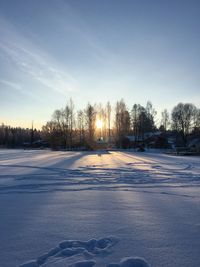 Snow covered field against sky during sunset