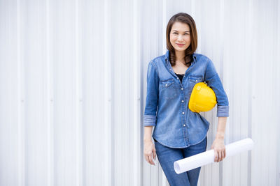 Portrait of a smiling young woman standing against wall