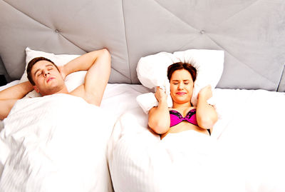 Woman covering ears with pillow while lying down by man on bed at home