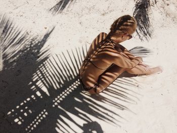 Shadow of palm leaf on woman sitting in bikini at beach