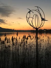 Silhouette plants by lake against sky during sunset