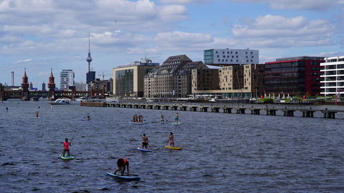 People on river by buildings in city against sky