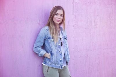 Beautiful young woman standing against pink wall