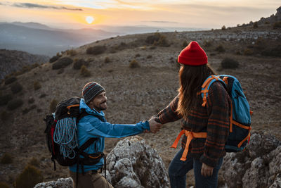 Girlfriend helping boyfriend to climb rocky mountain during sunset