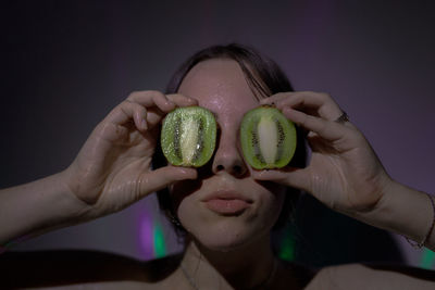 Close-up of woman covering eyes with kiwi slices in darkroom