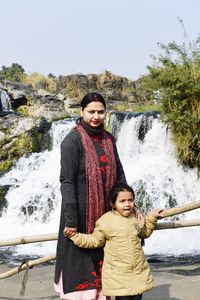 Portrait of smiling woman and her daughter  standing against waterfall in water