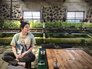 Side view of young man using mobile phone while standing in greenhouse