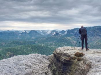 Photographer check display of camera on tripod. man stay on cliff and takes photos talk friends.