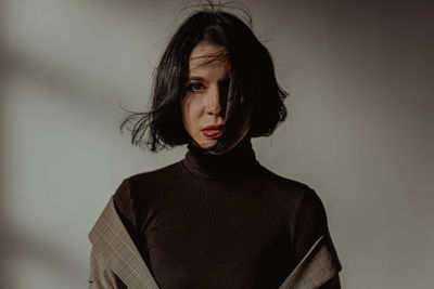 Tranquil female with flying hair and in black turtleneck looking at camera in room against white wall
