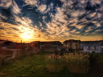 Houses on field by buildings against sky during sunset
