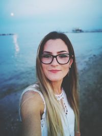 Portrait of smiling young woman wearing eyeglasses at beach during sunset