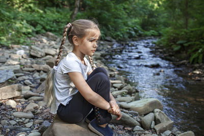 Full length of girl sitting on rock in forest