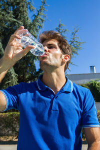 Midsection of man drinking glass against blue background