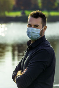 Portrait of man wearing mask standing against lake