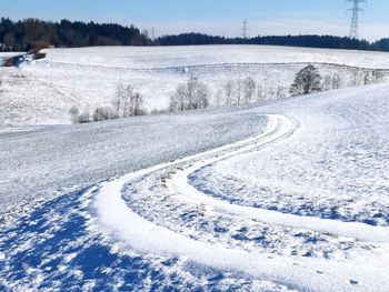 Snow covered road amidst trees on field during winter