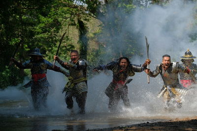 Male warriors with weapons running in lake at forest