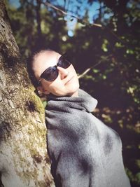 Portrait of young woman wearing sunglasses against tree trunk