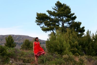 Rear view of woman standing by trees against sky