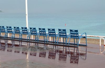 Empty blue metallic seats on promenade by sea