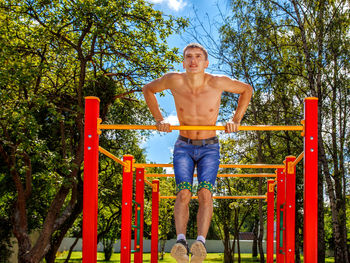 Shirtless young man hanging on play equipment at playground