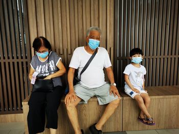 Grandparents with granddaughter wearing mask sitting on bench