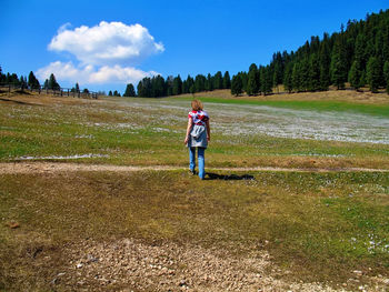 Rear view of woman walking on grassy field during sunny day