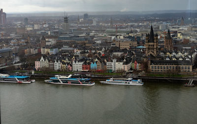 Sailboats in river by buildings in city against sky