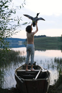 Rear view of boy holding bird against sky
