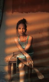 Portrait of woman sitting on seat against wall