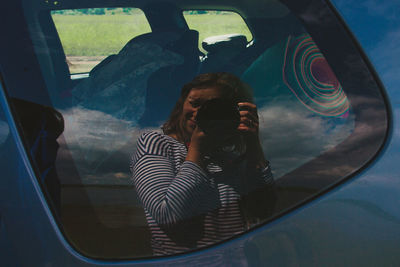 Reflection of woman photographing with camera seen on car window