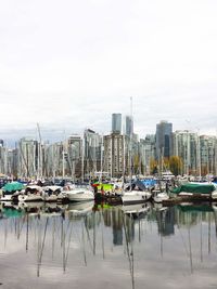 Boats moored at harbor against sky in city