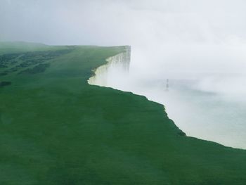 Scenic view of grassy cliff against sky during foggy weather