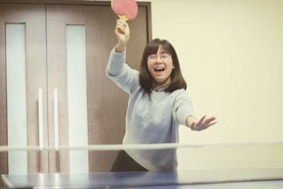 Cheerful young woman holding table tennis racket at home