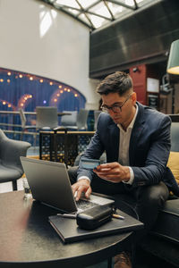 Male entrepreneur holding credit card while using laptop in hotel lounge