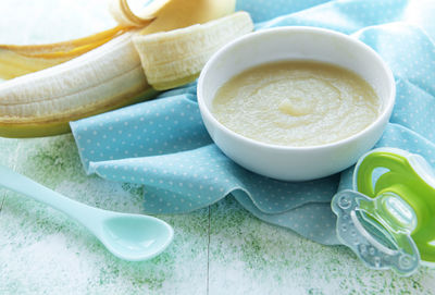 Bowl with baby food and banana on table