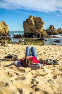Woman sitting on rock at beach against sky