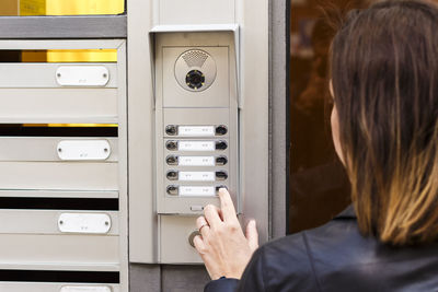 Rear view of woman using intercom on wall