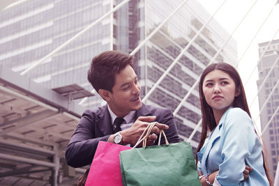 Boyfriend giving shopping bags to sulking girlfriend in city