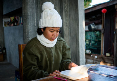 Concept of a female student in winter coat sitting alone reading a book on the balcony