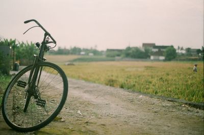 Bicycle on field by road against sky