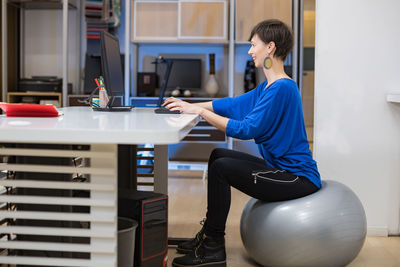 Young woman working on computer and sitting on pilates ball