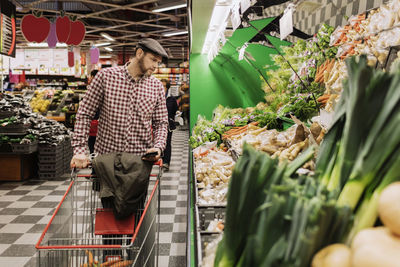 Man holding smart phone while choosing vegetables in supermarket