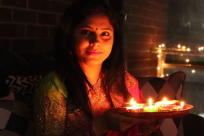 Smiling woman with burning diyas at home