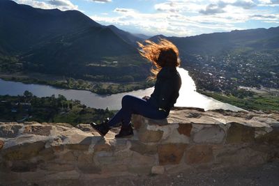 Full length of woman sitting by lake against mountains