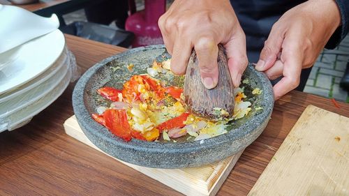 Cropped hand of person preparing food grinding the spices with a mortar and pestle from a stone