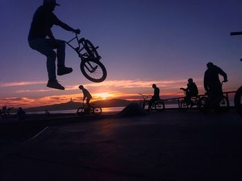 Silhouette people riding bicycles against sky during sunset