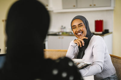 Happy young woman wearing hijab talking with friend at home