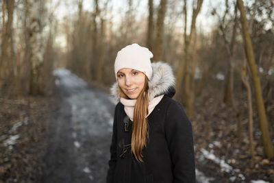 Portrait of young woman standing in forest during winter