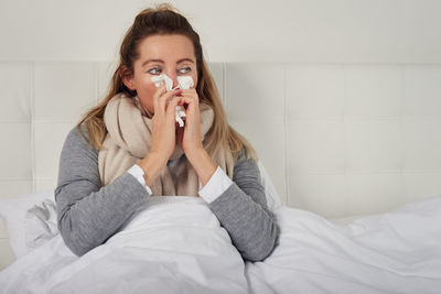 Sick woman sitting on bed at home