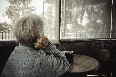 Rear view of old person sitting by window at home. concept loneliness, dementia, abuse, sadness.